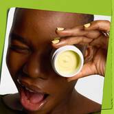 Model koji namiguje sa posudicom Kiehl's Creamy Eye Treatment sa avokadom koja prekriva jedno oko