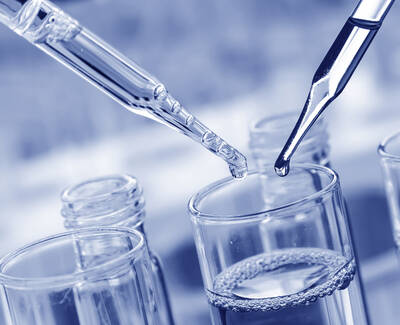 Two droppers are above glass test tubes with clear liquid, depicting a laboratory setting. The image has a blue tint.