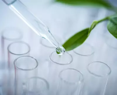 A dropper releasing a drop of liquid above several test tubes, with a green leaf in the background.
