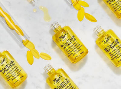Bočice Kiehl's Daily Reviving koncentrata sa žutim laticama na belom stolu, uz kapljice ulja.