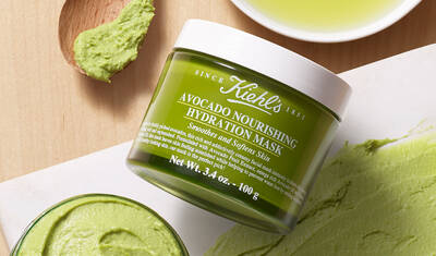 A jar of Kiehl's Avocado Nourishing Hydration Mask sits on a wooden surface, with a small scoop of the green mask and a puddle of olive oil nearby.