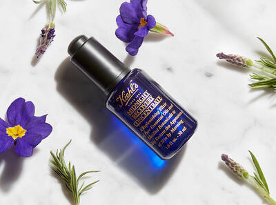 Mali plavi bočica hidratantnog seruma na beloj površini, okružena biljnim cvetovima.