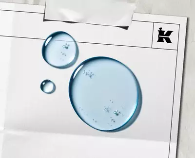 Plave kapljice tečnosti koje predstavljaju α-Bisabolol na belom listu sa crnim Kiehlovim logom u uglu.