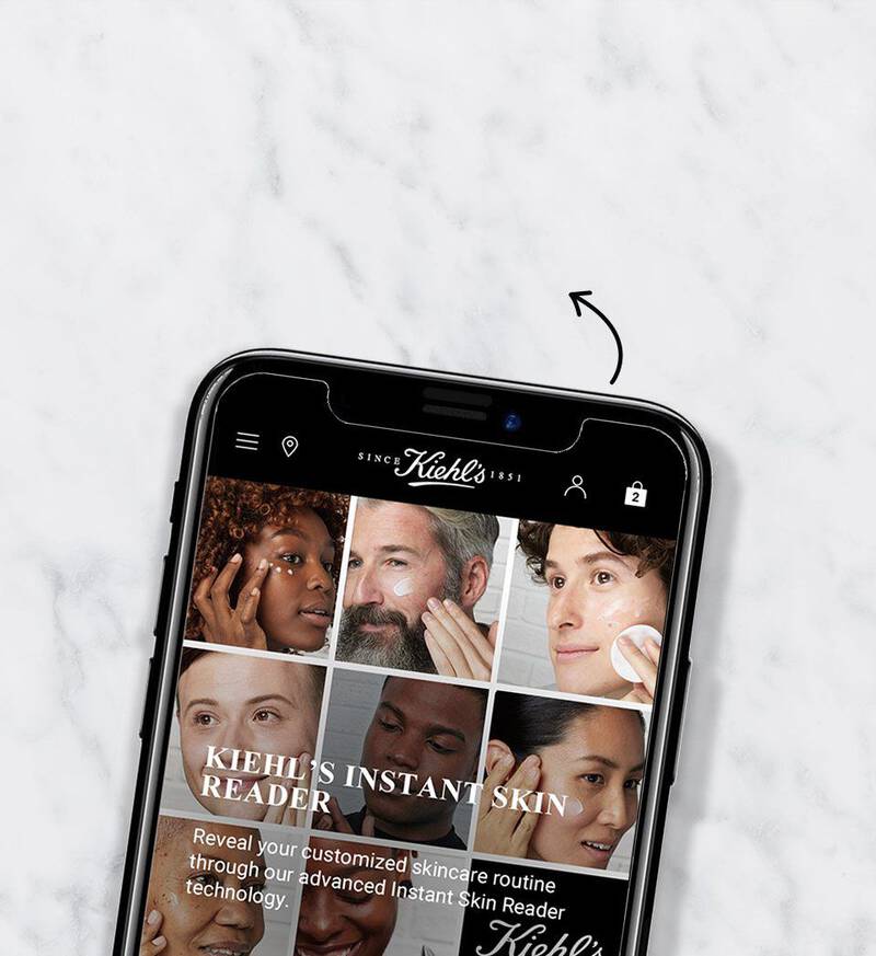 A smartphone displaying a beauty website on a marble surface. The screen features a grid of diverse faces showcasing various skincare products.