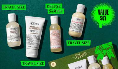 A flat lay image on a dark green background showcases a Kiehl's product set, highlighted with a bright green value price graphic. The set includes four travel-sized products: on the left, a 75ml bottle of Kiehl's Amino Acid Shampoo; next to it, a 75ml tube of Kiehl's Amino Acid Conditioner; in the center, a 65ml deluxe sample bottle of Kiehl's Bath and Shower Liquid Body Cleanser in 'Grapefruit' scent; and on the right, a 75ml bottle of Kiehl's Creme de Corps. A green Kiehl's gift box with a prominent ribbon graphic is partially visible in the bottom right corner of the image.