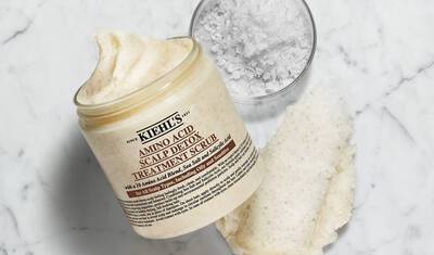 A jar of Kiehl's Amino Acid Scalp Detox Treatment Scrub, opened to reveal a creamy scrub, with a small bowl of salt nearby and a textured sponge alongside.