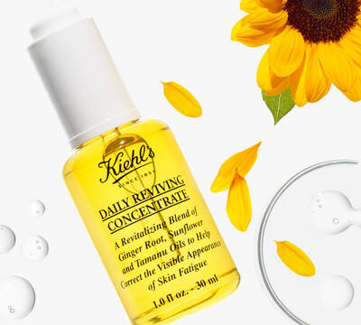Bočica Kiehl's Daily Reviving Concentrate, žute boje sa cvetovima suncokreta i kapljicama ulja, na beloj pozadini.