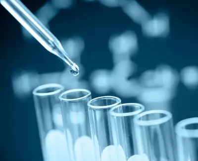 A pipette is about to drop a liquid into a row of clear test tubes, with a blurred DNA sequence graphic in the background.