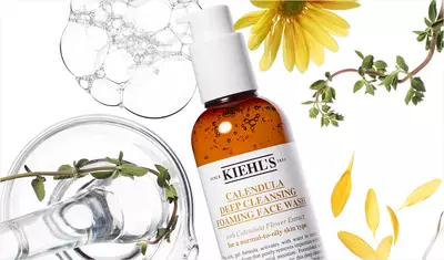 A bottle of Kiehl's Calendula Deep Cleansing Foaming Face Wash surrounded by fresh calendula flowers, herbs, and bubbles.