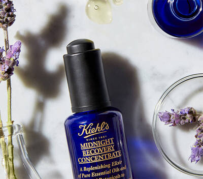 Plavi bočica Kiehl's Midnight Recovery Concentrate sa lavandom i eteričnim uljima na belom stolu.