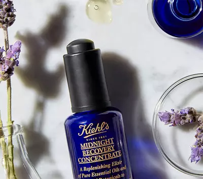 Plavi bočica Kiehl's Midnight Recovery Concentrate sa lavandom i eteričnim uljima na belom stolu.
