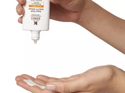 Osoba istiskuje kremu za sunčanje Kiehl's na dlan, spremna za nanošenje na kožu.
